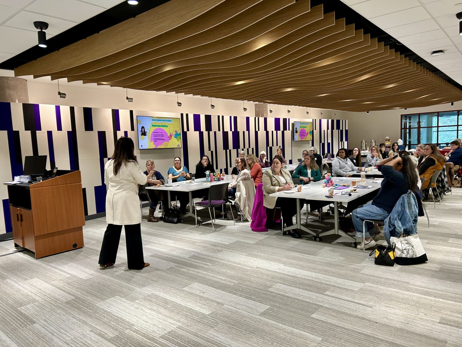 Photo of a person leading a workshop in a room full of people sitting at tables